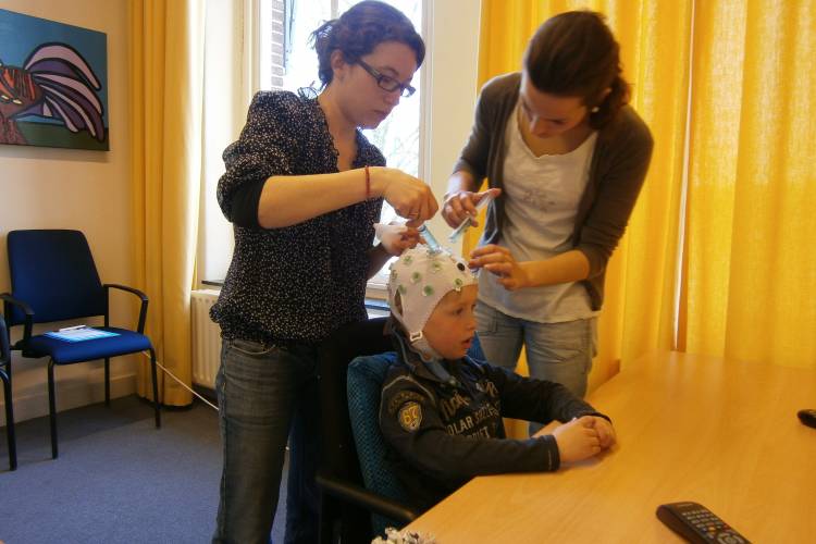 Twee volwassen vrouwen brengen EEG elektrodes aan bij een jongen